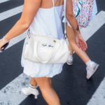Load image into Gallery viewer, Person walking on a street with a white handbag featuring branding.