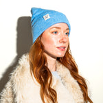 Load image into Gallery viewer, Woman wearing a blue beanie with a logo against a plain background