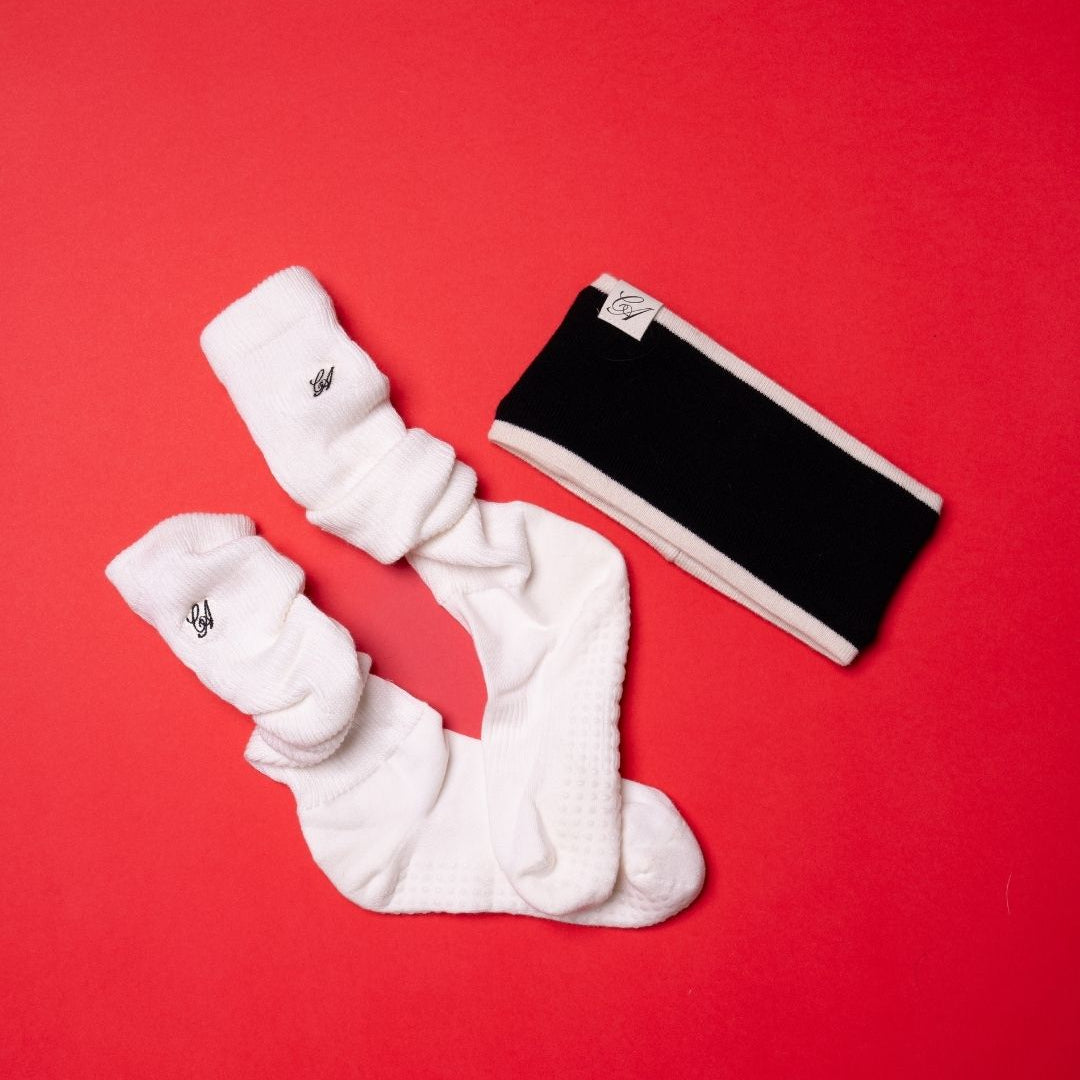A pair of white textured crew socks and a black knit headband with white trim, arranged on a solid red background.
