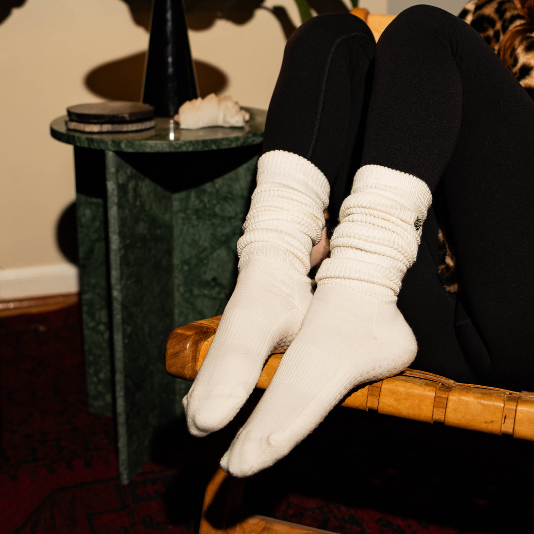Person wearing white socks sitting on a wooden chair with a small table in the background.