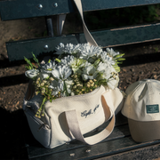 White floral arrangement in a bag on a bench with a cap beside it