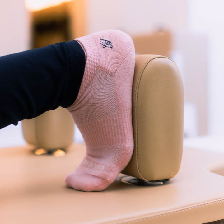 Person wearing pink socks with a brand logo, resting foot on a beige reformer.