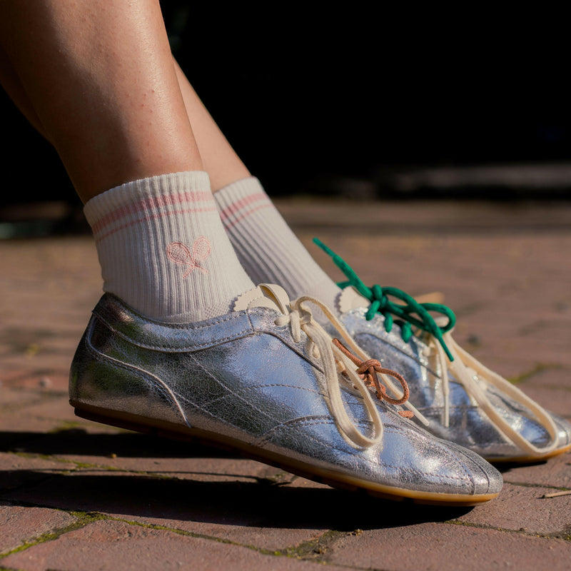 Blue sneakers with green laces worn on a brick surface