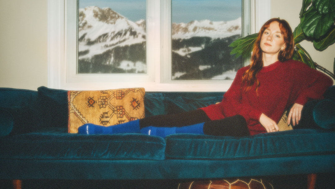 Woman sitting on a blue couch with a scenic window view in the background