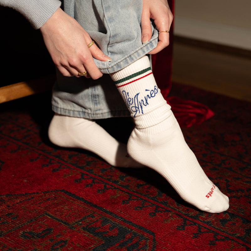 Person wearing white socks with colorful stripes and text, standing on a red patterned rug.