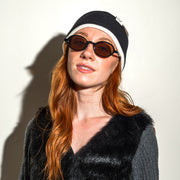 Woman wearing sunglasses and a black beanie against a white background